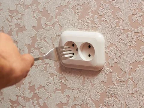 A person inserting a table plug into an electrical outlet is dangerous, it is Stock Photos