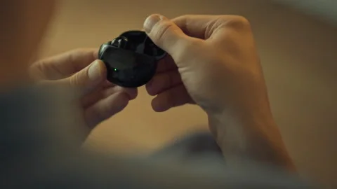 Person inspecting wireless earbuds in a cozy indoor setting Stock Footage 323869338