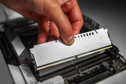 A person is installing a white DDR memory module into a desktop motherboard Stock Photos