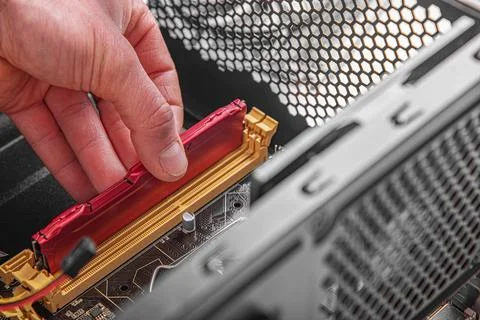 A person installs a red RAM module into the motherboard slot of a computer. Stock Photos