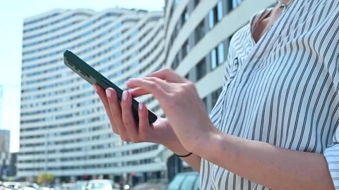 A person interacts with a mobile phone while standing in a busy urban area. The 库存影片 336778354