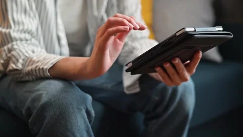 A person interacts with a tablet while seated on a couch in a living room. Their Stock Footage 338446168