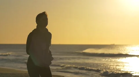 Person jogging exercising by beach with sun behind slowmo Stock Footage 53644142