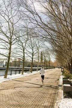 Person jogs along a tree-lined path by the river in winter, enjoying the fresh Stock Photos