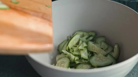 A person in a kitchen prepares cucumbers by cutting them and adding them to a Видео 338304127