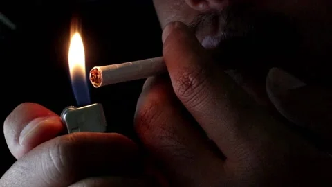 A person lights a cigarette using a gas lighter and inhales cigarette smoke. Stock Footage 220622656