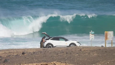 Person Loading Car by Ocean as Waves Crash Heat Haze Fuerteventura 스톡 동영상 331312555