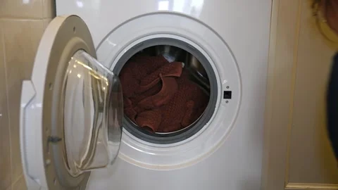 Person loading clothes into front load washing machine in laundry room Stock Footage 339664449