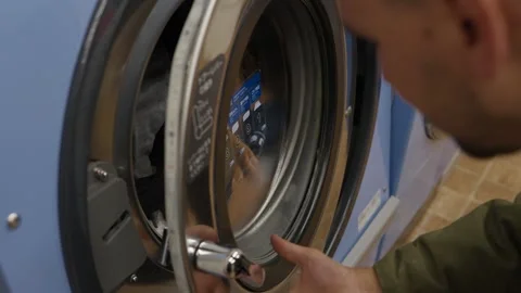 Person loading clothes into washing machine at laundromat Japan Видео 333382351