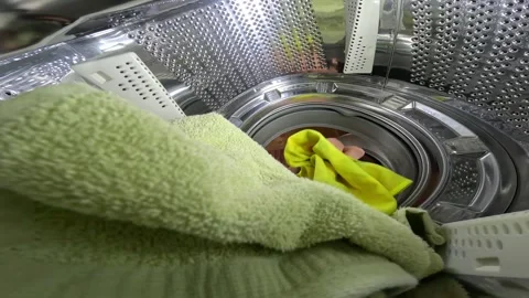 Person loading dirty laundry into the drum of a front-loading washing machine Stock Footage 346642341