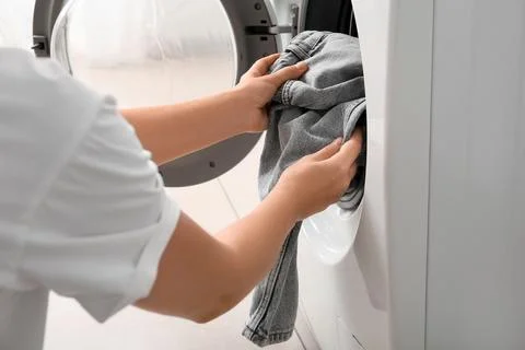 Person loading gray laundry into a modern front-loading washing machine for h Fotos de archivo