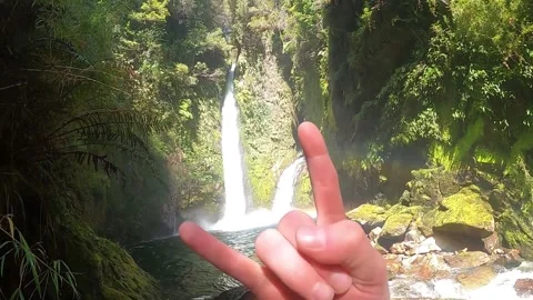 A person looking at a high waterfall in Chile and showing rock fingers Stock Footage 130662704