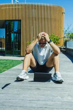 Person looks stressed while using a tablet outdoors near a modern building .. Stock Photos