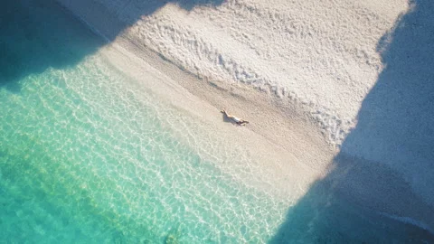 Person lying alone on pristine white beach with turquoise shallow water and tall Stock Footage 315434945