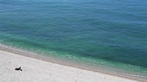 A person lying on a shingle beach and sunbathing near the ocean Stock Footage 45880286