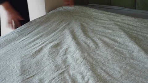 Person making bed with patterned blanket smoothing out wrinkles dynamic motio Stock Footage 332625815