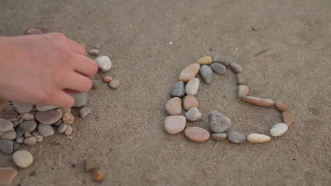 A person is making a heart shape with rocks on the beach Stock Footage 276481069