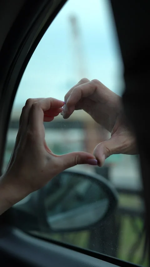Person making heart shape with their hands against car window during rides, Vidéo 342759469