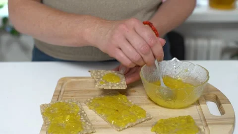 Person making snacks with toppings on crisp bread in a kitchen during the day Stock Footage 330654230