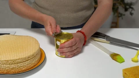A person is making a waffle cake by spreading condensed milk on wafers using a Stock Footage 336068508