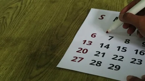 Person marking dates on a paper calendar with a red marker pen for scheduling Stock Footage 341956332