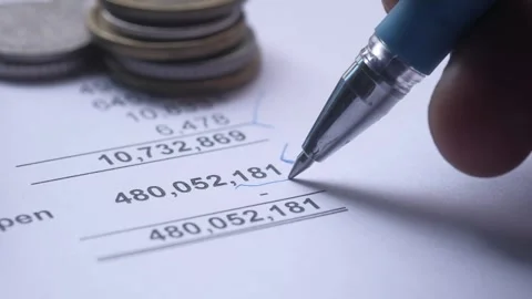 Person marking financial data on document with pen next to coins in slow mo.. Stock Footage 332473228