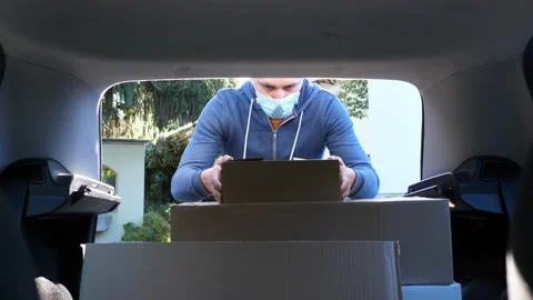 A Person in a Mask Puts Boxes in the Trunk of a Car Stock Footage 146606407