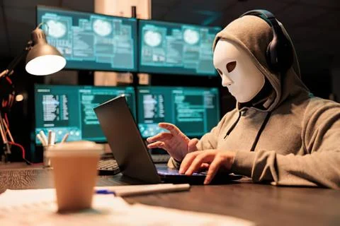 Person in mask using laptop in tech workspace Stock Photos