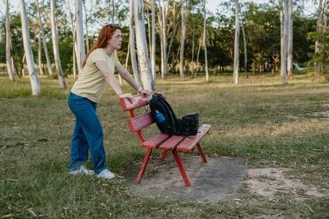 Person moving a red bench with backpack in a park, change and resilience Stock Photos