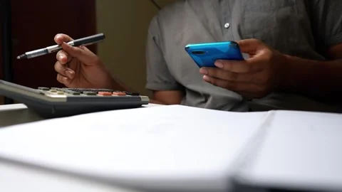 Person multitasking with smartphone, pen, and calculator Stock Footage 320725095