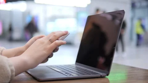 Person multitasks on phone and laptop in busy indoor area Stock Footage 342589083