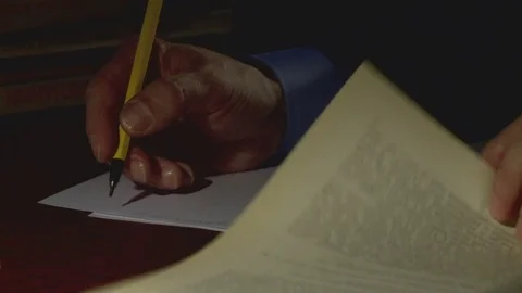 A person at night in the office at the table writes a pencil text on a sheet of Stock Footage 79418188