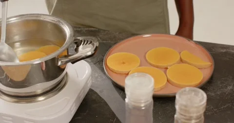 Person in olive-top scooping discs using spoon onto plate in kitchen, hot liquid Stock Footage 344105728