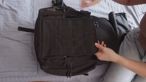 Person opening black tactical backpack zipper on bed closeup, travel prep Stock Footage 318774863