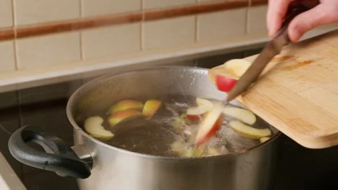 A person opens the lid of a pot of boiling water and puts the pieces of an apple Stock Footage 308157406