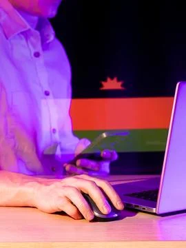 Person operating computer with red-black-green flag and rising sun overlay .. Stock Photos