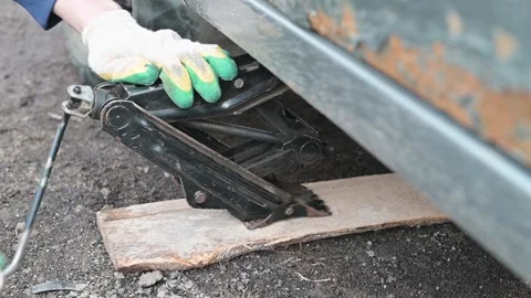 A person is operating a jack under a car while on an uneven surface. The focus Stockbeeldmateriaal 337550678