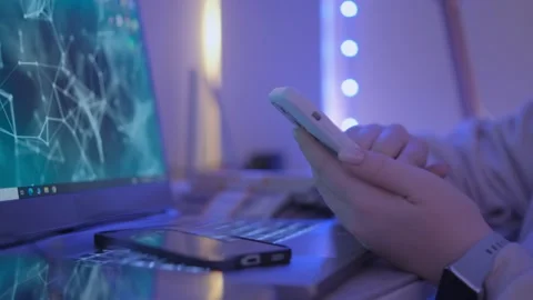 A person operating a smartphone on a desk surrounded by a computer and tech Stock Footage 276434966