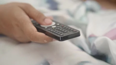 Person operating tv remote control lying in bed, changing channels in slow .. Vídeos de archivo 332194832