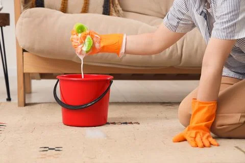 Person in orange gloves squeezing a soapy sponge into a red bucket while clea Stock Photos