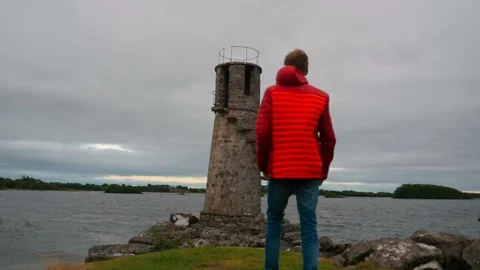 Person with orange jacket in front of old lighthouse in Ireland Stock Footage 100054575