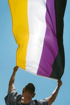 Person outdoors waves a non-binary pride flag Stock Photos