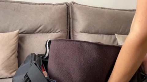Person Packing Folded Dark Clothes Into Duffel Bag on Sofa Vídeo Stock 345994506