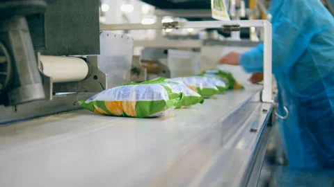 A person packs bags with potato crisps into a box, taking them from a conveyor. Stock Footage 104968583