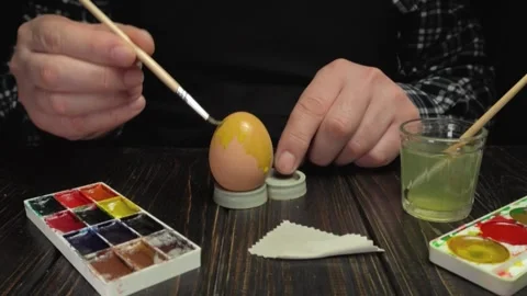 Person painting decorative patterns on an egg using a fine brush, with Stock Footage 338254466