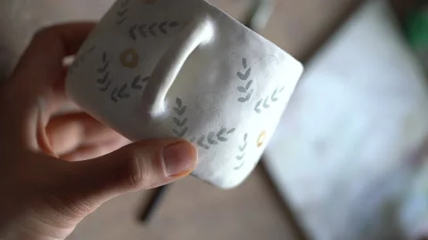 Person paints brown circles pattern on white ceramic mug in kitchen at home on Stock Footage 202223617