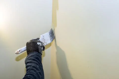 Person paints wall corner using brush wearing gloves in room with soft lighting Stock Photos