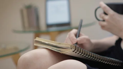 A person is peacefully jotting down notes in a notebook while holding a mug Stock Footage 276665907