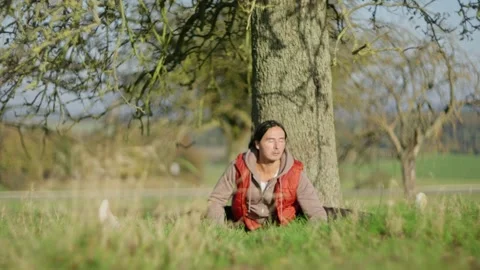 A person peacefully sitting under a tree in nature during the beautiful daylight Stock Footage 302658384