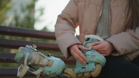 Person in Peach Jacket Preparing to Put on Rollerblades on Park Bench Stock Footage 285557384